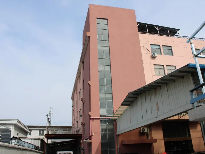 A large pink-colored industrial building with multiple floors and glass windows. The building has a distinctive architectural style with a tall vertical section and an attached lower structure. There are some industrial elements visible such as metal structures and equipment on the roof.